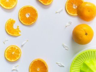 Sliced oranges on white background decorated with white leaves and hand juice extractor on corners