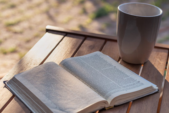 Christian worship and praise. The open bible on a chair in the morning light with cup of coffee.