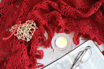 Crochet Red shawl. Lit candle, tea, Bible and glasses. Rest, autumn mood. Faith in God, Christianity. The concept of retirement age and quiet old age.