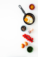Recipe of fried eggs with vegetables. Ready eggs in a frying pan near cherry tomatoes, greenery, spices, raw eggs on white background top view copy space