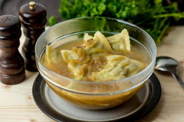 maultaschen, German, traditional dumplings in a bowl with onion soup, next to fresh parsley, salt shaker and pepper pot