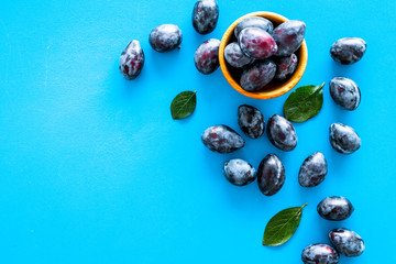 Plums on dinning table. Fresh raw purple plum in wooden bowl on blue background top view copy space