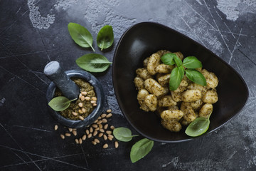 Potato gnocchi served with freshly made basil pesto sauce, flatlay over dark grey concrete background