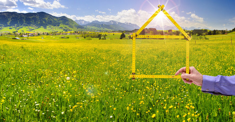 Makler hält Meterstab in Form von einem Haus als Symbol für Wohnen im Grünen
