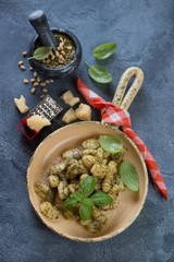 Serving pan with potato gnocchi, basil pesto sauce and parmesan cheese. High angle view over blue stone surface, vertical shot
