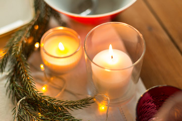 christmas, holidays and decoration concept - burning candles and fir branch on table served for festive dinner at home