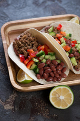 Close-up of tacos with ground beef meat, red beans and fresh vegetables on a wooden serving tray, vertical shot