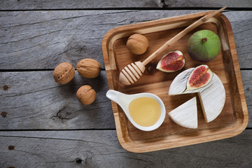 Wooden serving tray with camembert, fig fruits, honey and walnuts. Top view on a grey rustic wooden background