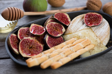 Close-up of a cast-iron serving pan with baked camembert cheese, slices of fig fruits, honey and salted breadsticks