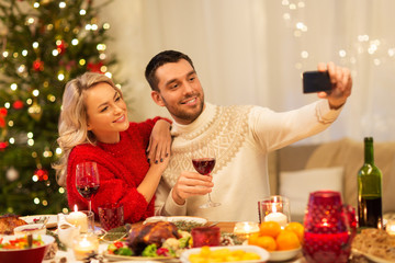christmas, holidays, technology and people concept - happy couple in taking selfie by smartphone at home dinner