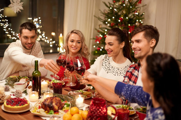 holidays and celebration concept - happy friends having christmas dinner at home, drinking red wine and clinking glasses