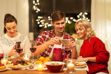 holidays and celebration concept - happy friends having christmas dinner at home and photographing food by smartphone