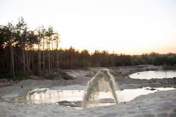 the water fountain beats out of the ground. sand alluvium. sand pit. river at sunset. extraction of sand