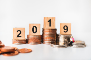 Miniature people, woman reading on stack coins with year 2019 using as business and financial concept