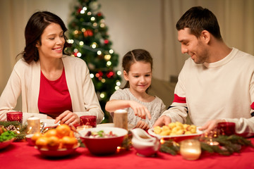 holidays, family and celebration concept - happy mother, father and little daughter having christmas dinner at home