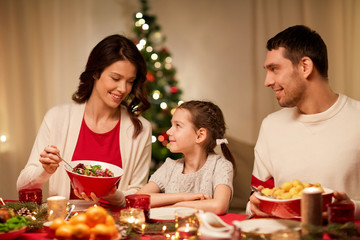 holidays, family and celebration concept - happy mother, father and little daughter having christmas dinner at home