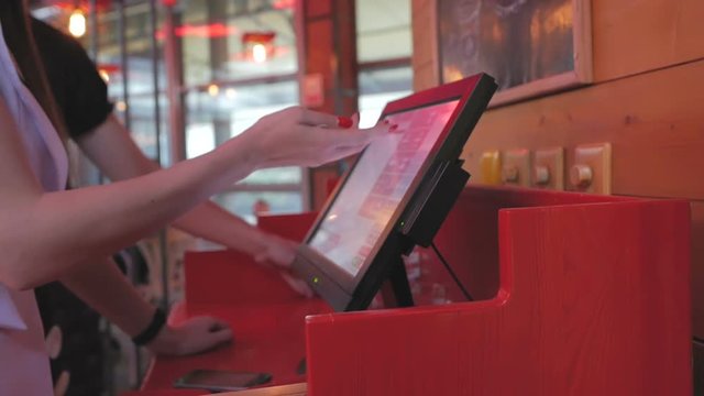 The waitress makes an order for the kitchen using a touch computer or POS system in the restaurant, pressing her fingers on the monitor screen.