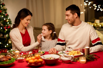 holidays, family and celebration concept - happy mother, father and little daughter having christmas dinner at home