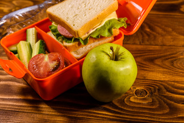 Bottle of water, green apple and lunch box with sandwich, cucumbers and tomatoes on wooden table