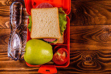 Bottle of water, green apple and lunch box with sandwich, cucumbers and tomatoes on wooden table. Top view