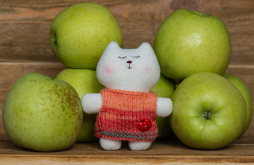 Closeup of green big sweet apples and a small toy cute cat on wooden table. small world. toys and vitamins
