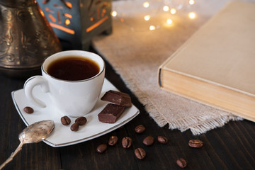 Cup of coffee with dark chocolate on dark background with book and bokeh lights - 224748485