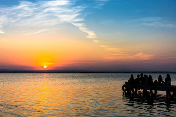 Fototapeta na wymiar People sitting on a dock enjoying the summer sunset on a beautiful lake. Amazing sky in color 
