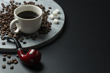 close up of a cup of coffee with a pile of coffee beans and the sugar cubes on the round marble...