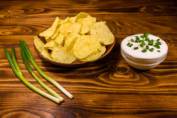 Ceramic plate with potato chips and glass bowl with sour cream on wooden table