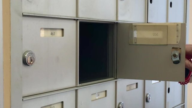 Elderly woman opens mail box with a key to find no mail