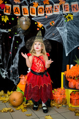 A child, a little girl in the shape of a witch on a broomstick, poses against the backdrop of scenery of cobwebs, pumpkins and autumn leaves on a Halloween holiday.