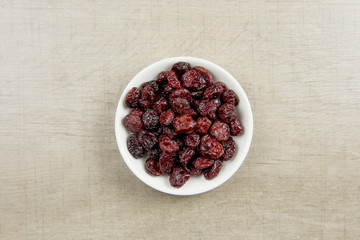 Dried cranberries in white bowl on gray wooden background.