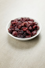Dried cranberries in white bowl on gray wooden background.