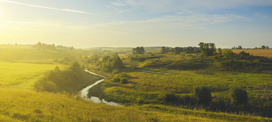 Sunny summer landscape with river flowing between the beautiful green hills,fields and meadows.