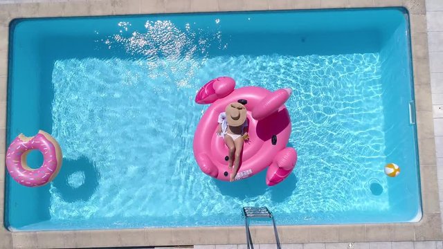 Aerial - Young woman relaxing on a giant pink flamingo float in the pool at home
