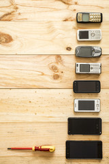 Several old and new mobile phones with screwdriver placed on wooden background