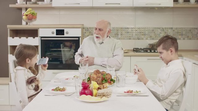 Grandpa Communicates With Grandchildren At The Table Before A Family Dinner
