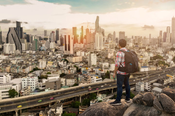 Young tourist standing on the top of mountain peak and looking  over a big city,copy space.