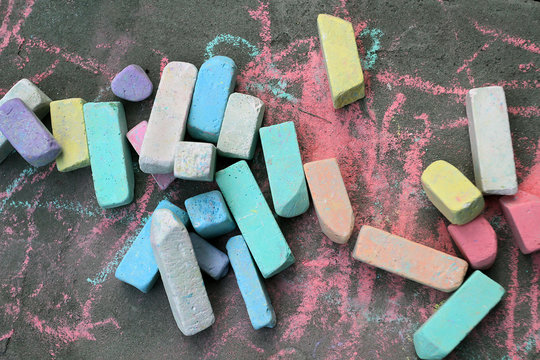 Many colorful chalks lie on the gray asphalt. Child creativity is not in the room, but in the street.