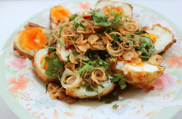 Fried boiled eggs with sweet and sour sauce topped with fried garlic, red onion and cilantro ( selective focus on center of eggs)
