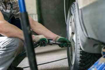 car mechanic screwing or unscrewing car wheel of lifted automobile at repair service station