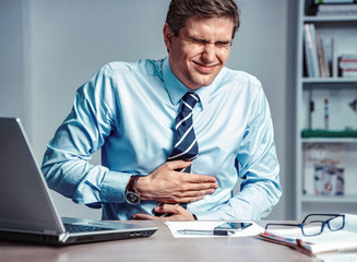 Fototapeta premium Employee suffers from severe pain in stomach. Photo of man working in the office. Medical concept.