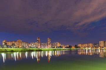 Fototapeta premium Night cityscape of residential buildings and park with a pond in the urban outskirts