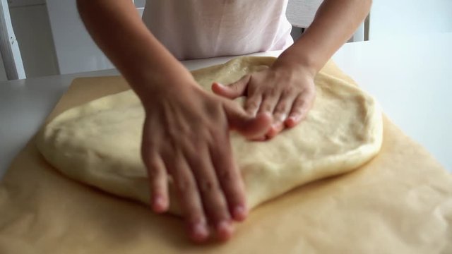 Baby hands close-up on a pizza dough 4k video. The child rolls a pancake dough for baking with his hands.
