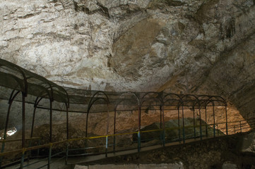 Dark cave view from inside with a lumen. Stalactites and stalagmites inside the stone grotto. Colorful stones in the cave. Lighting electricity beauty of the cave.