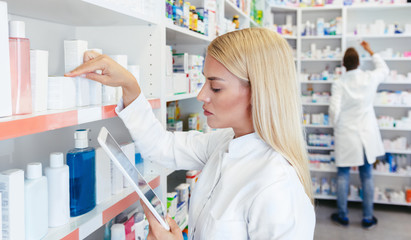 Woman pharmacist checking a medicine while holding a tablet in pharmacy drugstore - obrazy, fototapety, plakaty