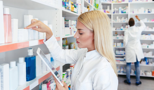 Woman pharmacist checking a medicine while holding a tablet in pharmacy drugstore