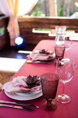A plate decorated with a succulent and a napkin on it, forks and knives, wine glasses beside it