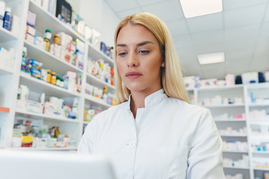 Beautiful young woman pharmacist at work looking at computer at pharmacy drugstore