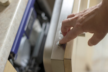 Hands pressing buttons on the dishwasher, making settings before machine starts.